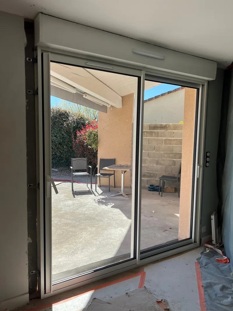 Grandes portes coulissantes vitrées avec cadres aluminium foncés s'ouvrant sur terrasse extérieure