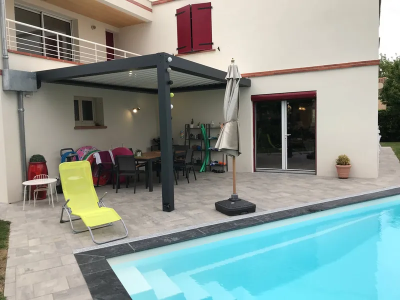 Pergola bioclimatique avec lames orientables au-dessus de terrasse avec piscine et chaise longue