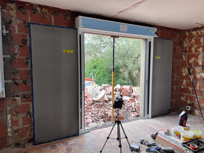 Rénovation intérieure avec grandes portes coulissantes en verre et cadres aluminium donnant sur zone de construction extérieure